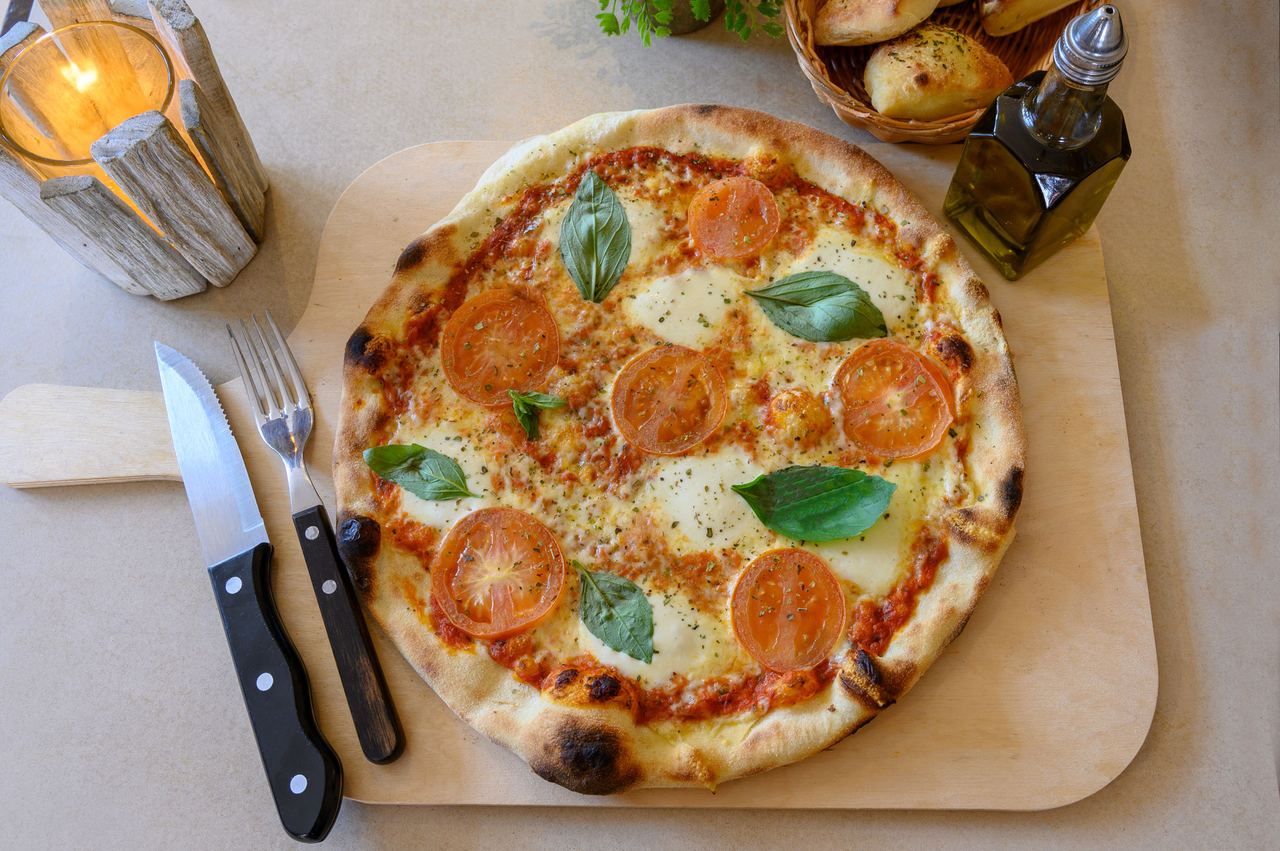 Pizza mit Tomatenscheiben und Basilikum auf einem Holzbrett